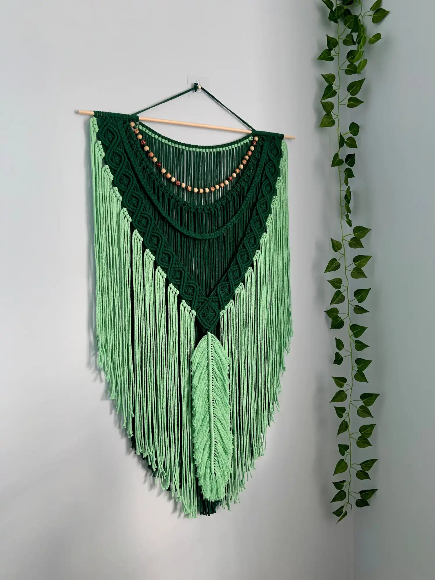 Green macrame wall hanging with beads on a white wall